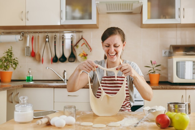 La joven divertida alegre y sonriente se pone una masa con agujeros en la cara y se divierte en la cocina. Cocinar en casa. Prepara comida.