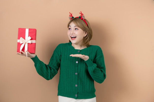 Una joven divertida y encantada con un disfraz de reno navideño riéndose con un regalo de fondo beige