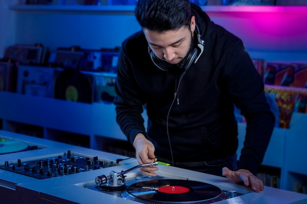 Foto joven dj colocando un disco de vinilo en un tornamesa para mezclar musica en una tienda de discos