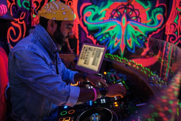 Joven DJ con pañuelo tocando música en un colorido club nocturno Concepto de mezcla de música vida nocturna
