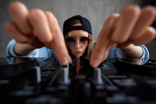 Una joven dj de pelo largo con un suéter azul y una gorra de béisbol negra posa con una mezcla de dj negra