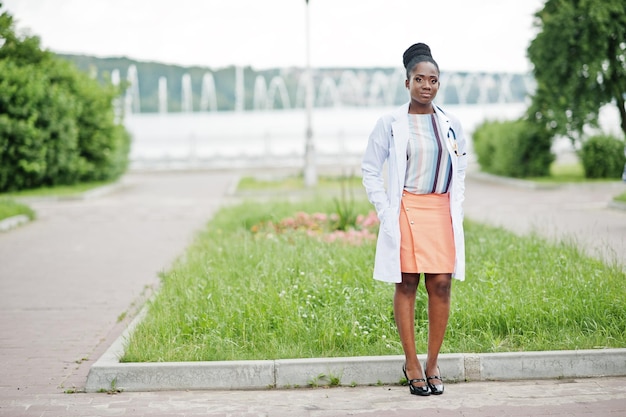 Joven doctora afroamericana en bata blanca con un estetoscopio posado al aire libre