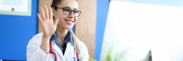 Joven doctora de belleza caucásica hablando con el paciente contra el retrato de la oficina del hospital. Concepto de educación médica a distancia