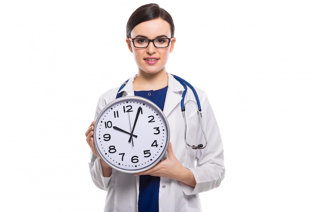 Joven doctora con estetoscopio con reloj en sus manos en uniforme blanco sobre blanco