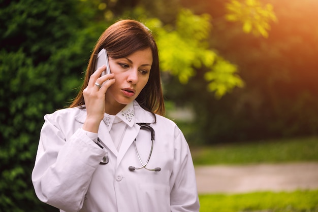 Joven doctora hablando por teléfono al aire libre