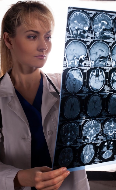 Joven doctora inteligente con bata blanca mirando a través de la resonancia magnética del cerebro humano