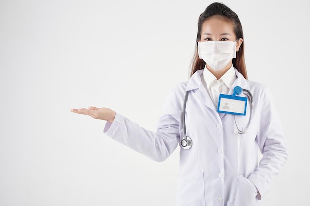 Joven doctora en máscara protectora y bata de laboratorio sosteniendo algo en la mano aislado en blanco