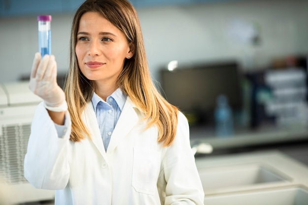 Joven doctora con mascarilla protectora en el laboratorio con matraz con muestra líquida