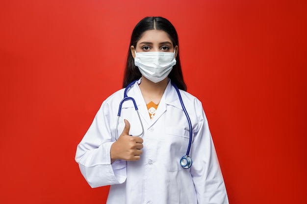 Joven doctora mirando al frente con máscara sobre fondo rojo modelo paquistaní indio