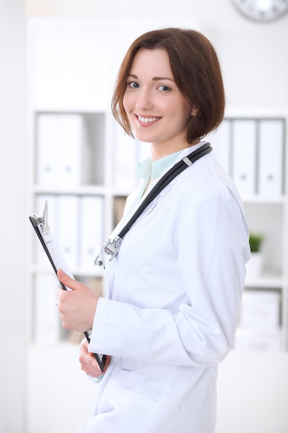 Joven doctora morena de pie con los brazos cruzados y sonriendo en el hospital. Concepto de atención médica, seguro y ayuda. Médico listo para examinar al paciente