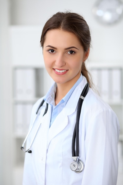 Joven doctora morena de pie con los brazos cruzados y sonriendo en el hospital. Concepto de atención médica, seguro y ayuda. Médico listo para examinar al paciente