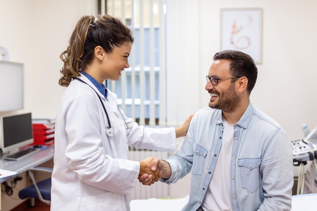 Una joven doctora o médico de cabecera con uniforme médico blanco consulta a un paciente masculino en un hospital privado Terapeuta femenina habla con un cliente masculino en consulta en la clínica