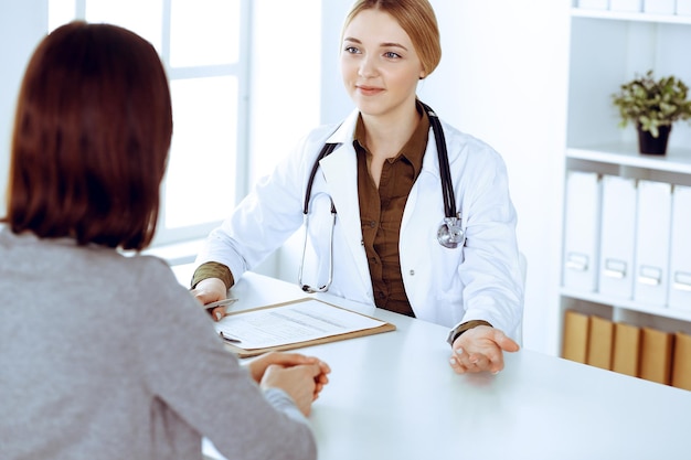 Joven doctora y paciente en un examen médico en el consultorio del hospital. Se ve bien la blusa color caqui de terapeuta. Medicina, atención médica y concepto de cita médica.