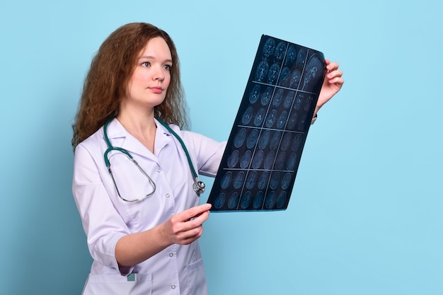 Foto joven doctora de pelo rizado en una bata médica blanca examina una imagen de resonancia magnética del cerebro en azul