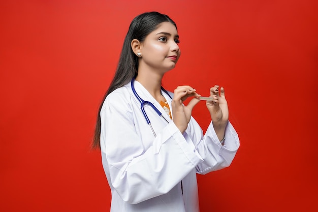 Joven doctora pose lateral sosteniendo el tubo de ensayo sobre fondo rojo modelo paquistaní indio