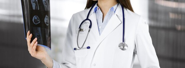 Una joven doctora profesional está mirando la radiografía de su paciente en la clínica. Concepto de medicina durante la pandemia de Coronavirus.