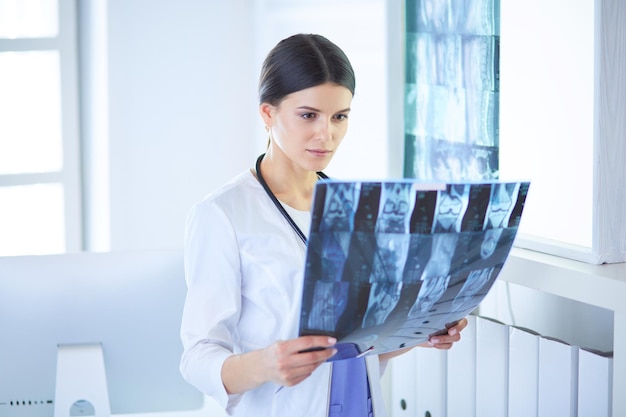 Joven doctora sonriente con estetoscopio mirando Xray en el consultorio del médico