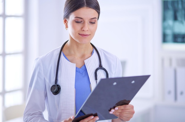 Joven doctora sonriente con estetoscopio sosteniendo una carpeta en el consultorio del médico