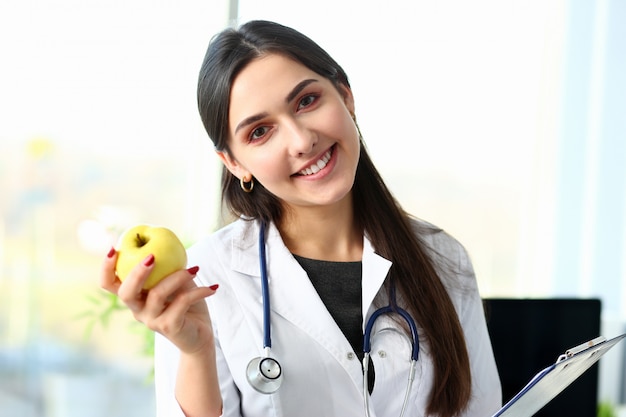 Joven doctora sonriente tiene manzana