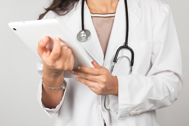 Joven doctora sosteniendo una tableta aislada en fondo gris