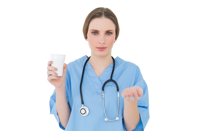 Joven doctora sosteniendo un vaso de plástico y presentando con su mano