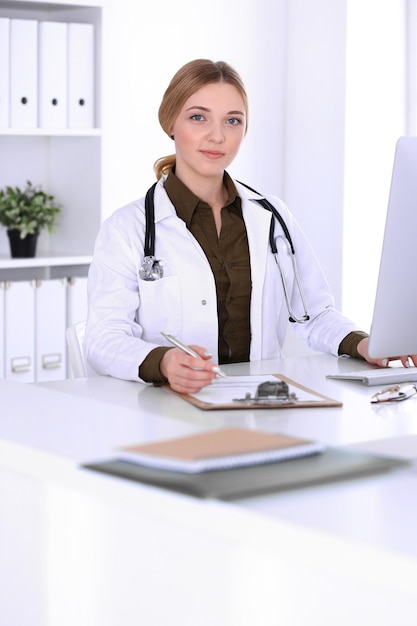 Joven doctora en el trabajo en el hospital mirando el monitor de pc de escritorio. El médico controla los registros del historial de medicamentos y los resultados de los exámenes. Concepto de medicina y salud.