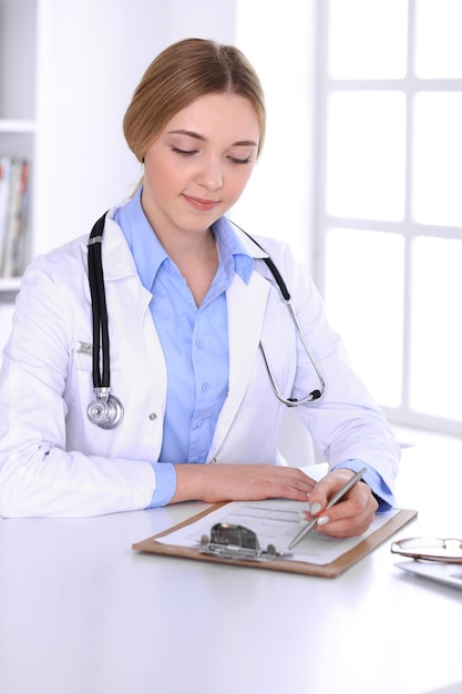 Joven doctora en el trabajo mientras llena los registros del historial de medicamentos en la oficina del hospital. El médico controla los resultados del examen. Concepto de medicina y salud.