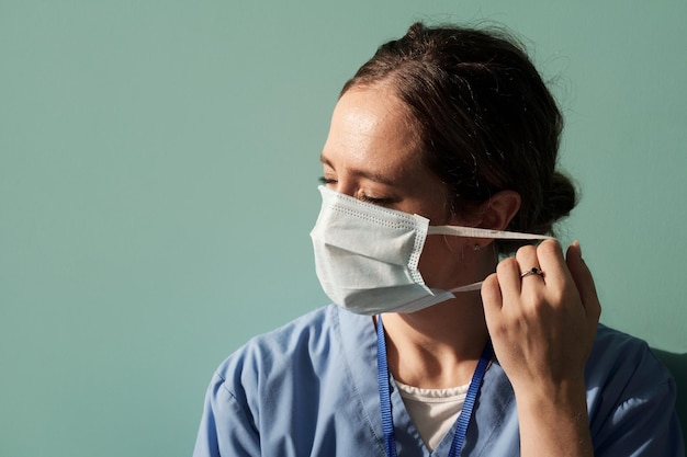 Joven doctora en uniforme va a quitarse la máscara protectora