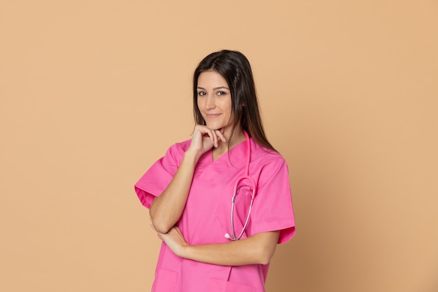 Joven doctora con un uniforme rosa gesticulando sobre pared marrón