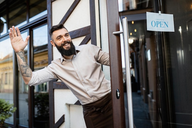 Foto joven dueño feliz del bar abriendo la puerta de entrada y saludando a alguien