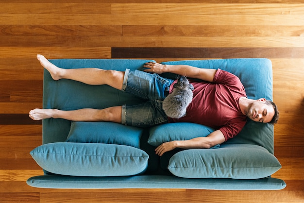 Joven durmiendo en el sofá en casa con conejito