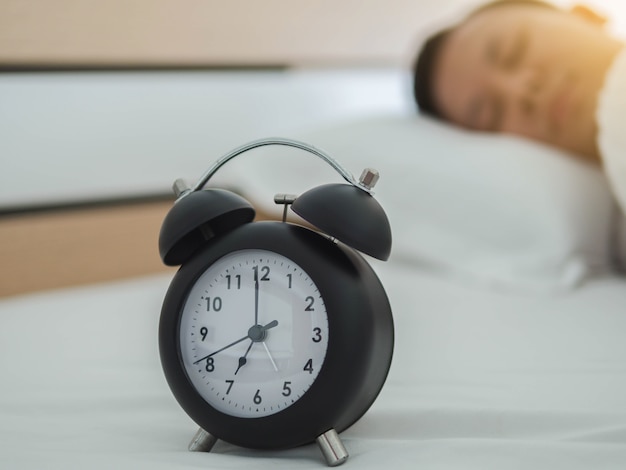 Foto joven durmiente y despertador en el dormitorio en casa