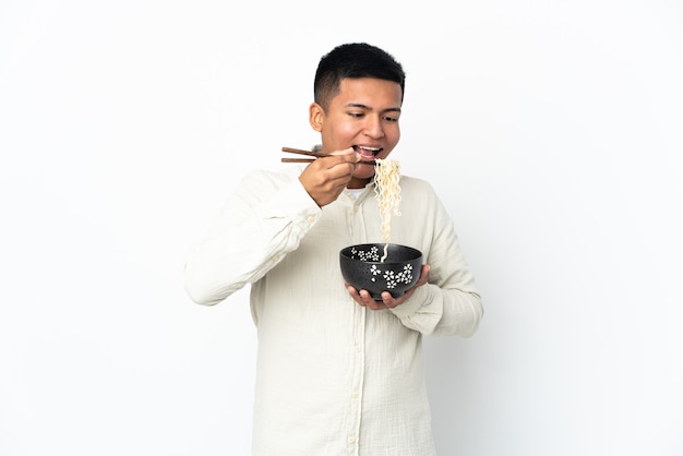 Joven ecuatoriano aislado sobre fondo blanco sosteniendo un plato de fideos con palillos y comiéndolo