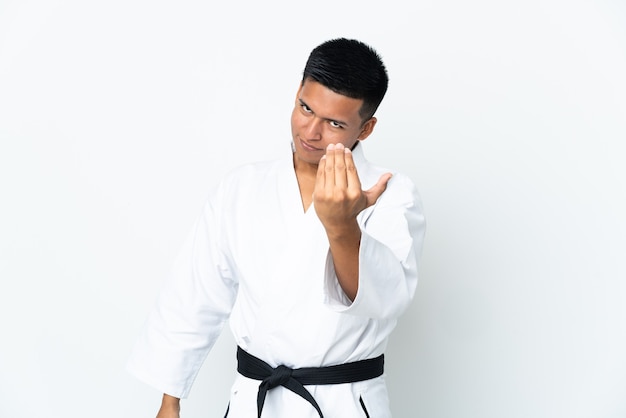 Joven ecuatoriano haciendo karate aislado en la pared blanca invitando a venir con la mano. Feliz de que hayas venido