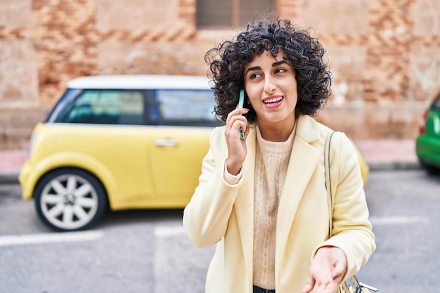 Joven ejecutiva de Oriente Medio sonriendo confiada hablando por el teléfono inteligente en la calle