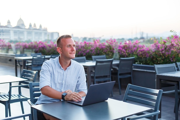 Un joven ejecutivo exitoso mirando sentado en una mesa con una laptop en la terraza de un hotel y encontrando tiempo para el control remoto de los empleados mientras estaba de vacaciones en un resort exótico