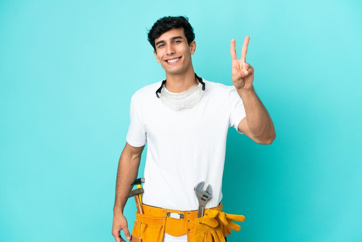 Foto joven electricista argentino aislado de fondo azul sonriendo y mostrando el signo de la victoria