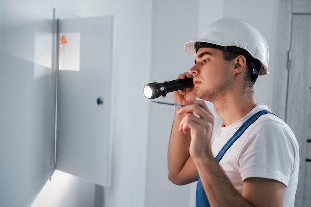 Un joven electricista con casco blanco trabaja en el interior de la habitación