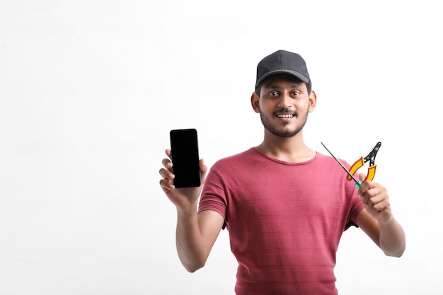 Joven electricista indio sosteniendo herramientas en la mano y mostrando el teléfono inteligente.