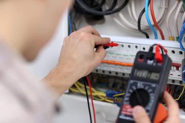 Foto joven electricista midiendo voltaje en tablero de fusibles