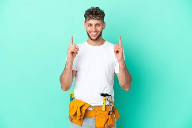 Joven electricista rubio aislado de fondo verde señalando una gran idea