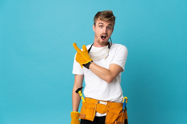 Foto joven electricista sobre pared aislada sorprendido y apuntando hacia el lado