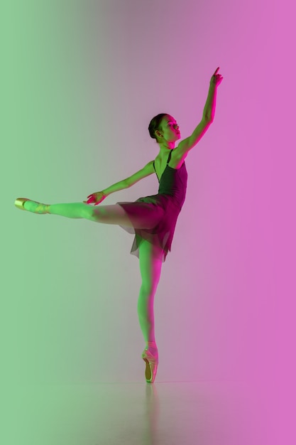 Joven y elegante bailarina de ballet aislada sobre fondo degradado de estudio rosa-verde