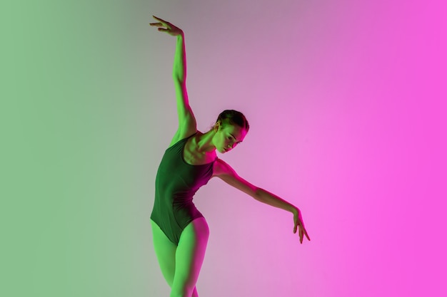 Joven y elegante bailarina de ballet aislada sobre fondo degradado de estudio rosa-verde