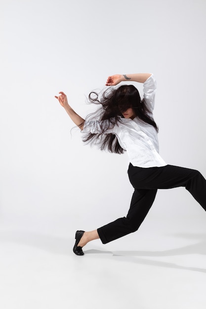 Foto joven y elegante bailarina de ballet en estilo minimalista negro aislado sobre fondo blanco de estudio. arte, movimiento, acción, flexibilidad, concepto de inspiración. bailarina de ballet caucásica flexible, saltos ingrávidos.