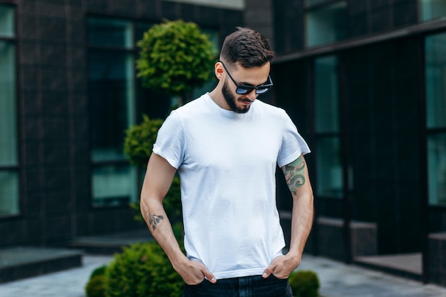 Un joven elegante con barba en una camiseta blanca y gafas de sol