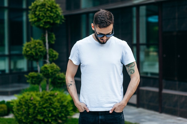 Un joven elegante con barba en una camiseta blanca y gafas de sol