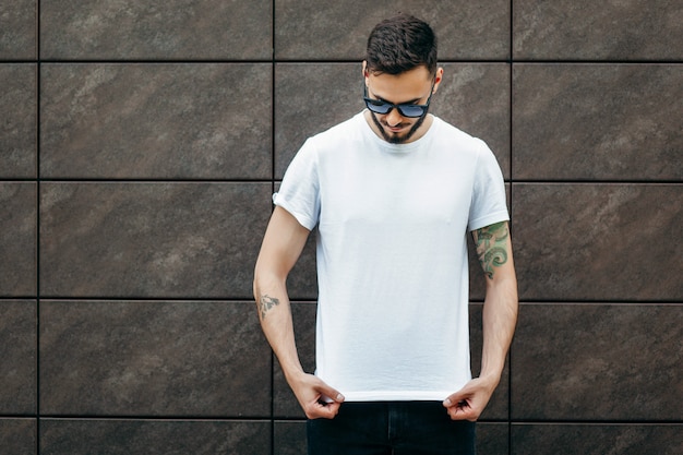 Un joven elegante con barba en una camiseta blanca y gafas de sol