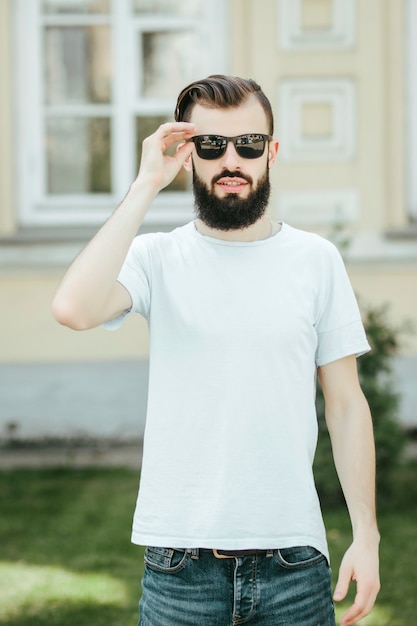 Un joven elegante con barba en una camiseta blanca y gafas