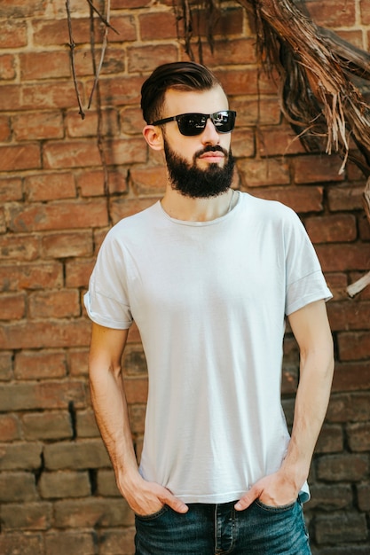 Un joven elegante con barba en una camiseta blanca y gafas